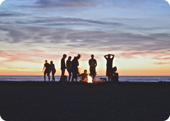 silhouette of young people at sunset around a fire on the beach